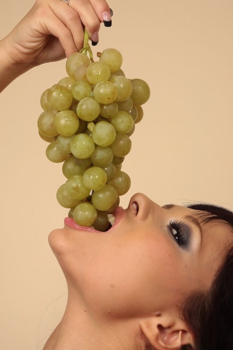 Hot brunette Domino munches on a grape bunch while removing her clothes