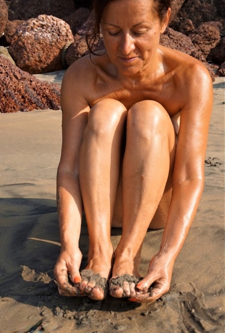 Naked older woman Diana Ananta covers her feet in beach sand at low tide